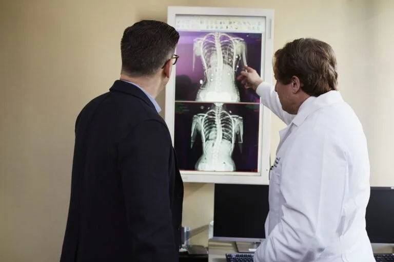 Médico e paciente observam radiografias da coluna