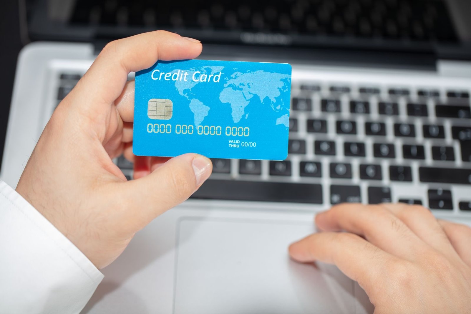 Person holding credit card near laptop for online shopping, emphasizing secure online tran