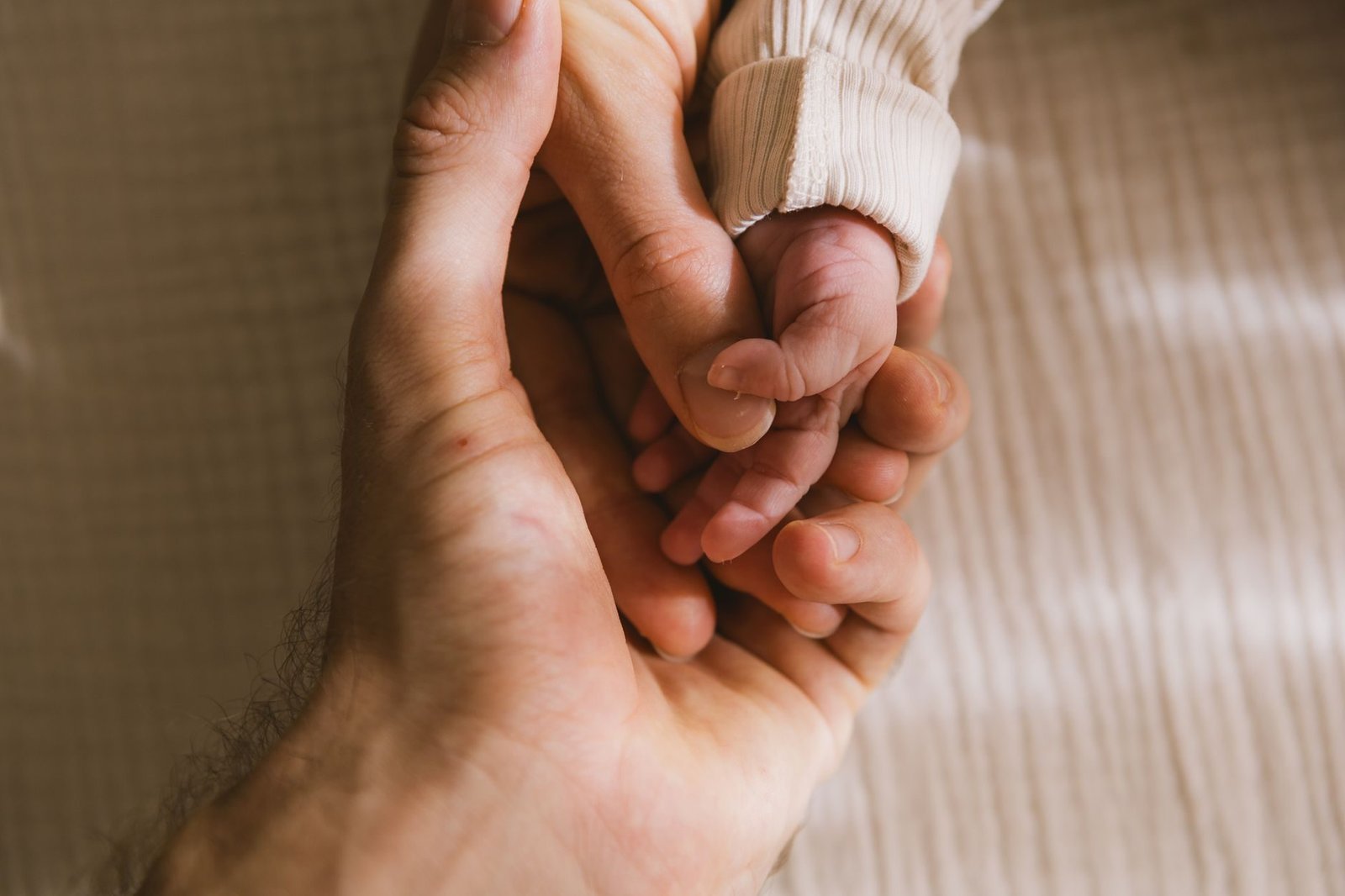 Mão de adulto segurando a mão de um bebê