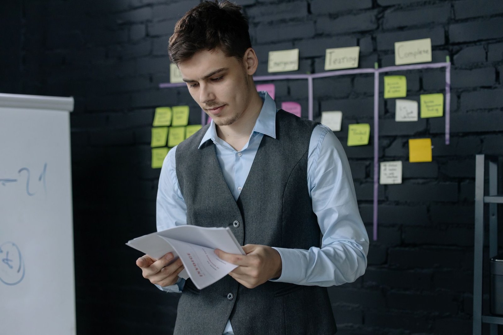 Trabalho intermitente: complemento para manter a carência 1 A young man reviewing documents in an office with a black brick wall and sticky notes back