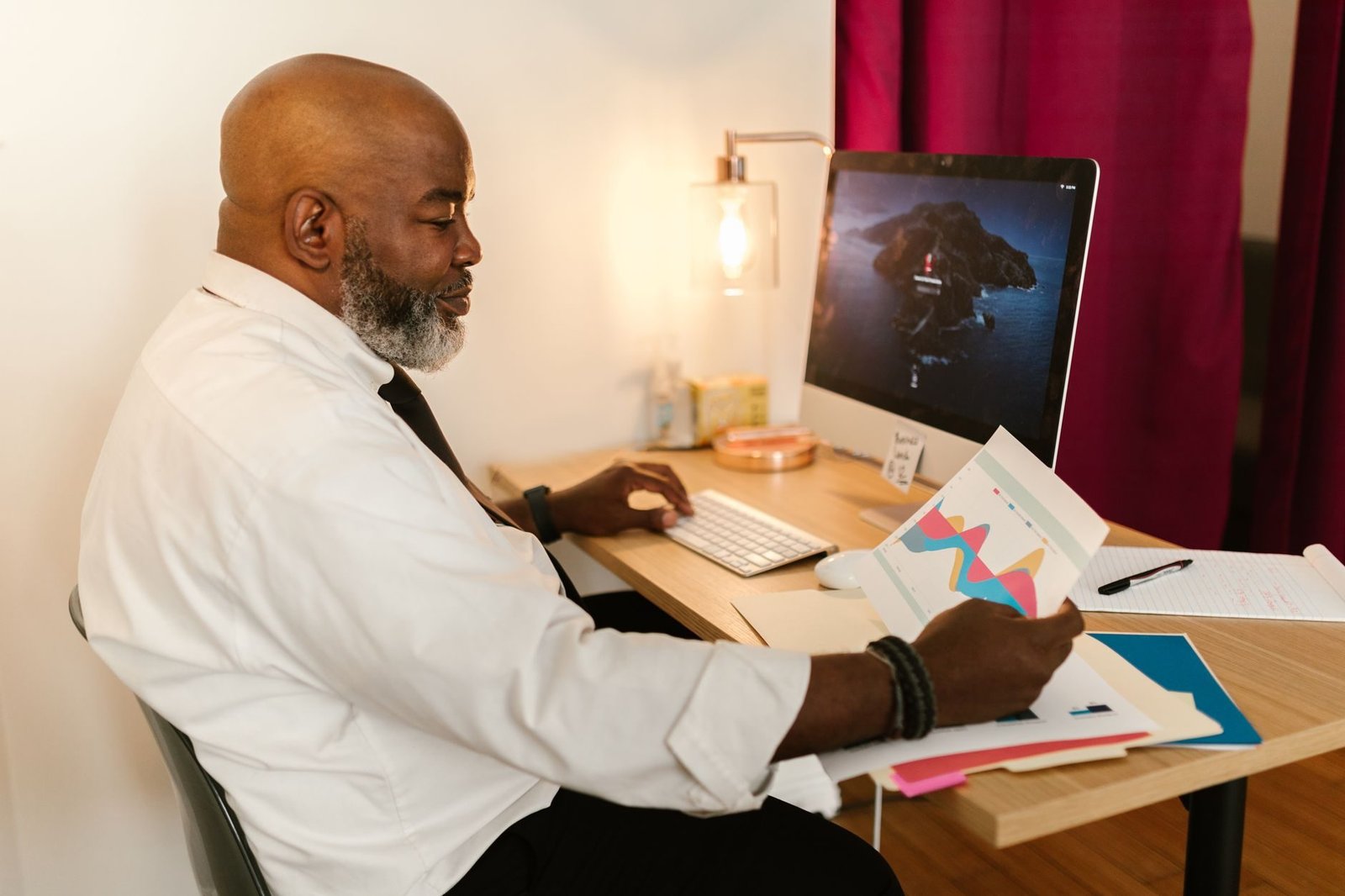 Homem de barba grisalha trabalhando diante de um computador de mesa