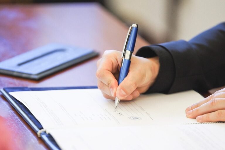 Mão assinando um documento com caneta sobre a mesa de escritório
