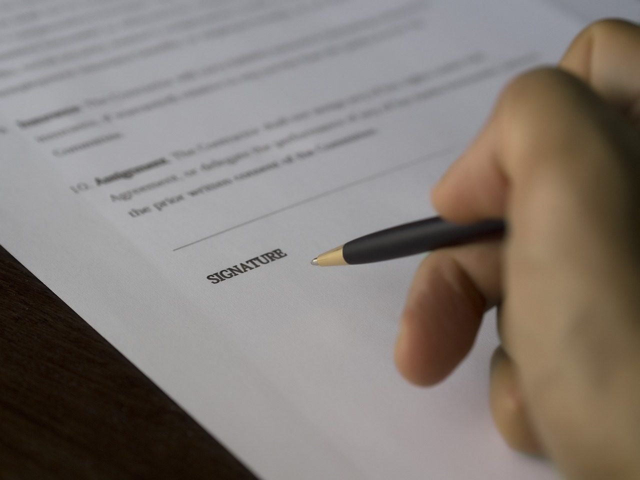 Mão com caneta sobre a linha de assinatura de um contrato